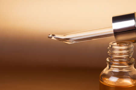 Cosmetic pipette close-up and bottle of cosmetic product, oil or hyaluronic acid on a gold background.の写真素材