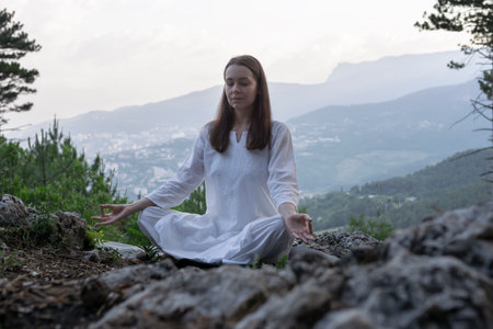 Beautiful young woman practices yoga and meditates on the mountain. Calmness and unity with nature.の写真素材
