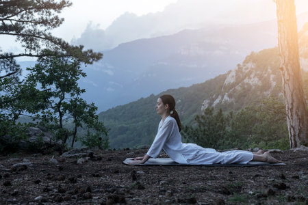Beautiful young woman practices yoga and meditates on the mountain. Calmness and unity with nature.の写真素材