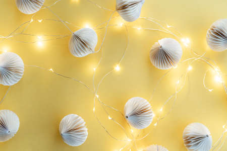 Christmas balls made of paper and a luminous garland with many lights on a yellow background. Winter...