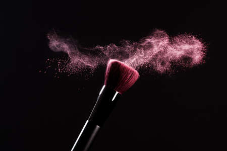Makeup brush with pink powder splashes explosion on black background. Beauty concept. Cosmetic background.の写真素材