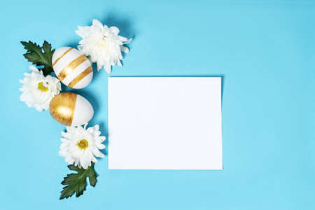 Hand-drawn easter eggs and spring white flowers on blue pastel background. Many easter eggs flat lay...