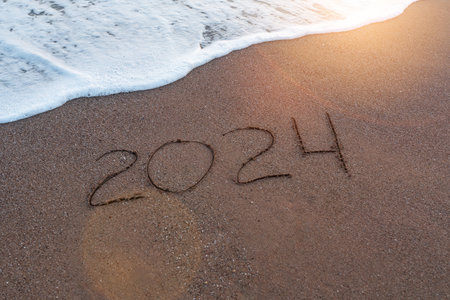 New Year 2024 is written by hand on the surface of the sand on the seashore or ocean. Freedom to relax and travel in the new yearの写真素材