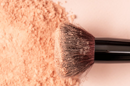 Makeup brush and loose beige powder against a background of sun glare. Powder texture, cosmetic...