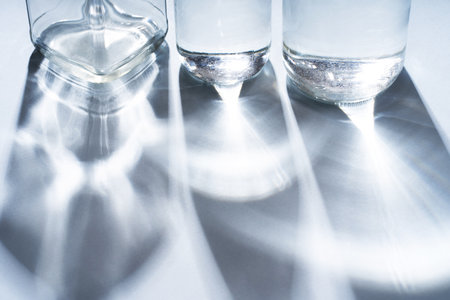 Glass bottles of different shapes with water on a blue background with long sunny shadowsの写真素材