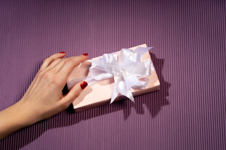 Female hands holding a gift box on a bright background. Gift for Christmas, Valentine's Day,...