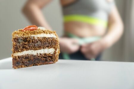 a piece of cake on the background of a girl measuring her waistの写真素材