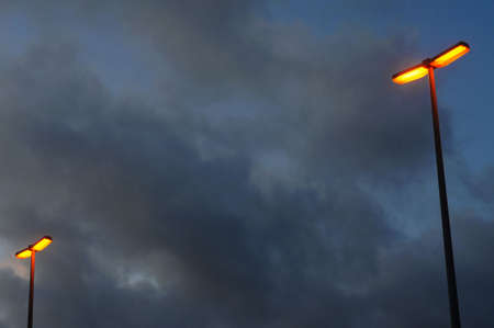 Orange glowing streetlamps under a stormy, cloudy skyの写真素材