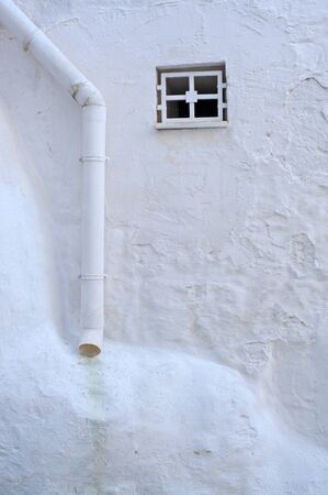 small window and drainpipe in white plastered wall in ostuni, italy, europe, room for your textの写真素材