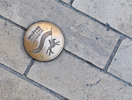 Small round copper plate on the streets and pavements of Orleans, France, with the name of the city in different languages and abstract image of Joan of Arc on her horseの写真素材