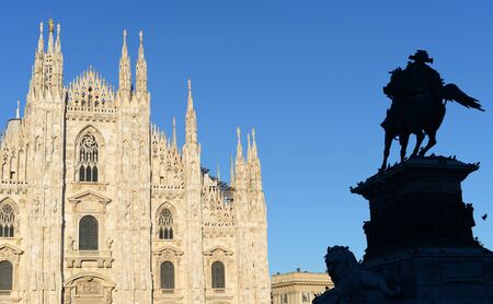 Milan duomo or cathedral against bright blue summer sky with silhouette of king Victor Emanuel covered in dovesの写真素材