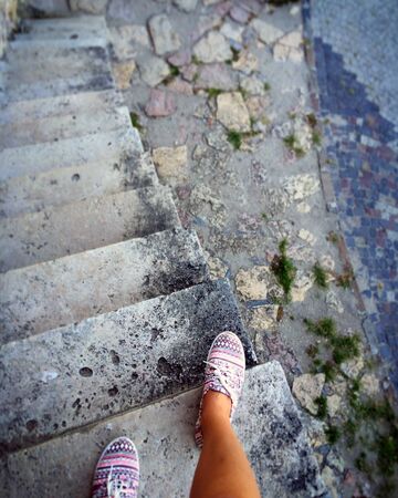 Descent on the stone steps. A look from above. In the frame, a ladder and legs in sneakers.