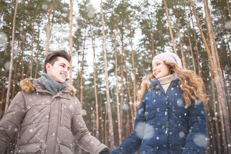 Couple walking in a winter forest, laughing, snowing
