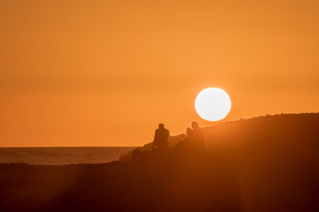 sunset at sea with silhouettes of people on the mountainの写真素材