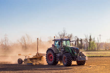 Tractor working in the field, preparing the land for planting, working plowed fieldの写真素材