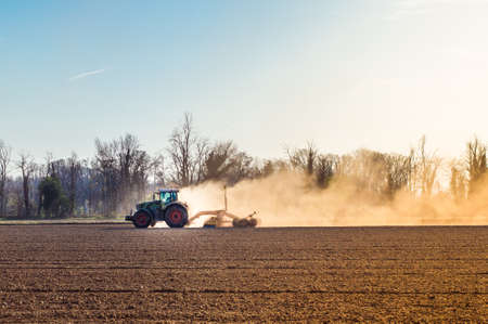 Tractor working in the field, preparing the land for planting, working plowed fieldの写真素材