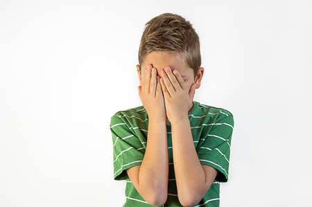 the ffightened boy covers his face with his hands on a white backgroundの写真素材