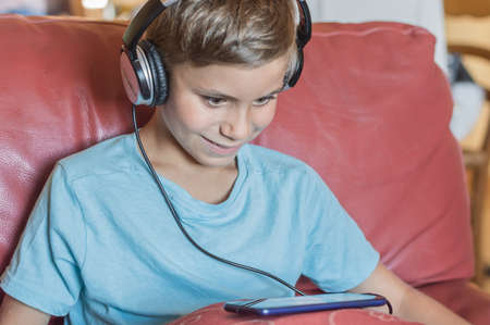 the boy is smiling and listening to music, playing, doing homework online with smartphone.Pupil in headphones.back to schoolの写真素材
