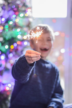 Selective focus happy boy is holding a burning sparkler on festive lights background.の写真素材