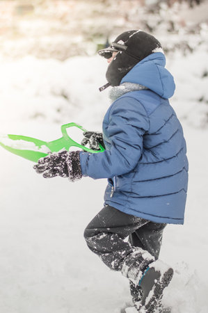 the child clears the snow with a shovel on the streetの写真素材