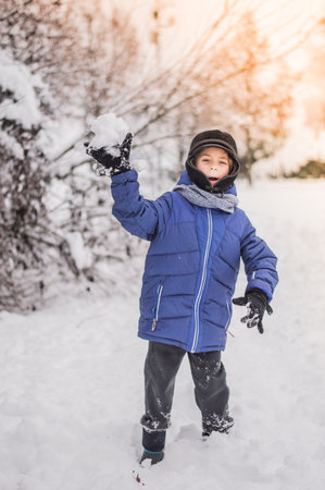 The child plays snowballs against the background of a snow forest.の写真素材