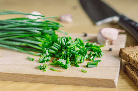 chropped green onions on a wooden board and garlic, bread, pepper and knife.