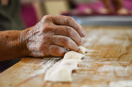 Hands of an old woman preparing ravioli pasta. Close up on wood backgroundの写真素材