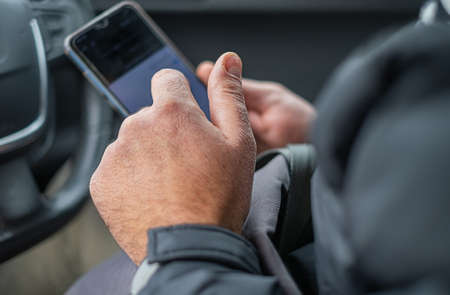 Male hands holding smartphone behind the wheel on the car