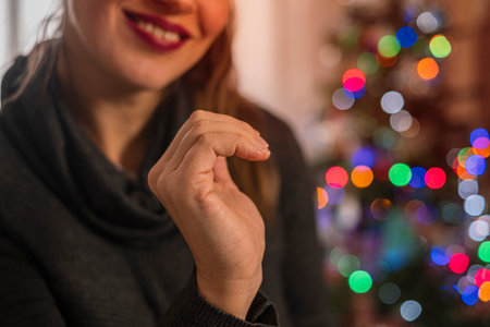 Cropped view smiling girl making a half of heart symbol with her hands. Blurred Christmas tree on background.の写真素材