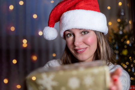 Smiling Woman in Santa hat with new year gift in background of lights.の写真素材