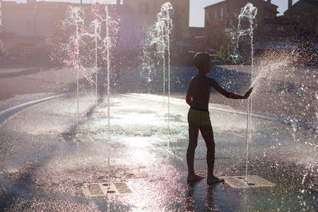Children in the city in summer in abnormally hot weather splash and have fun in the stone fountain. Boy play in spray of water.の写真素材
