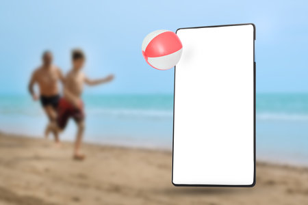 Mobile phone screen on the sandy beach with running people in backgroundの写真素材