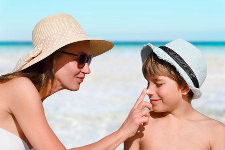 Woman carefully smears her childs face with protective cream on the beach. Skin care. Protection from the sun. Sunscreen for children.の写真素材