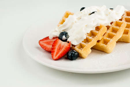 Belgian waffles with whipped cream and strawberry on a white plate.