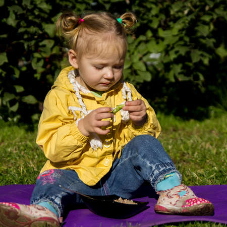 little hungry girl sitting on a grass and eating green peas.の写真素材