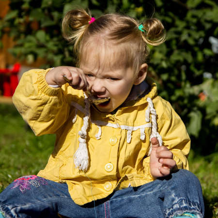 little girl is sitting on the grass and eating porridgeの写真素材