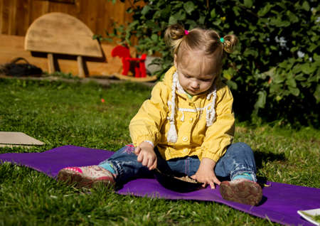 little girl is sitting on the grass and eating porridge.の写真素材