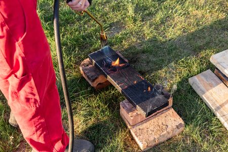 A man burns wooden planks with propane using old-time Japanese technology, creating facing material...