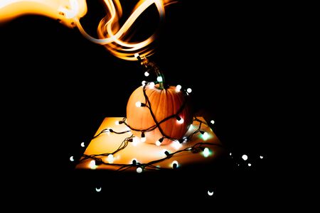 big round pumpkin in the bright lights of a garland on a black background