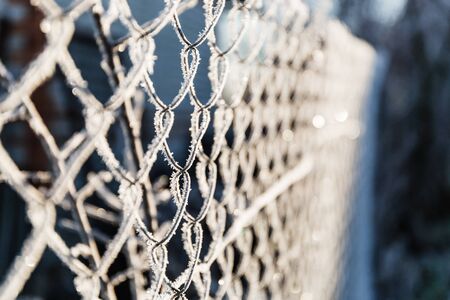 Beauty metallic chain fence link net with blue defocused background. Frosty winter day with bright sunlight.の写真素材