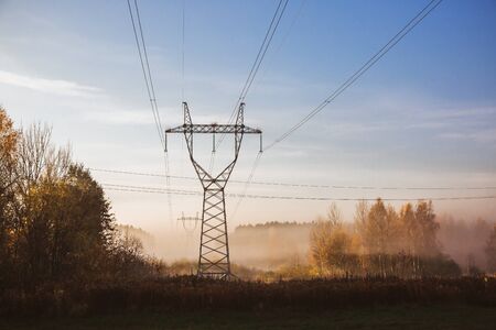 Electric transmission lines with electricity in the foggy morning autumn forest. Power lines.