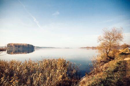Landscape of a sunny autumn day on a lake with a forest island reflected in the waterの写真素材