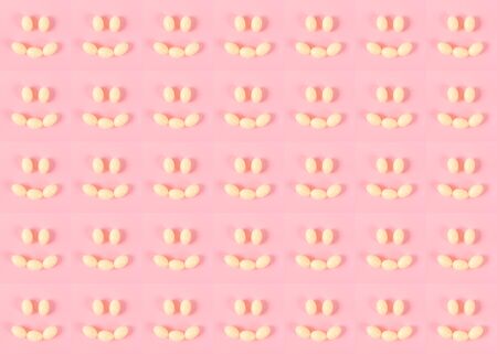Pattern of many small smiley emoticons made up of pills or eggs on a pink background. Happy emotions. Psychological help. Good day.の写真素材