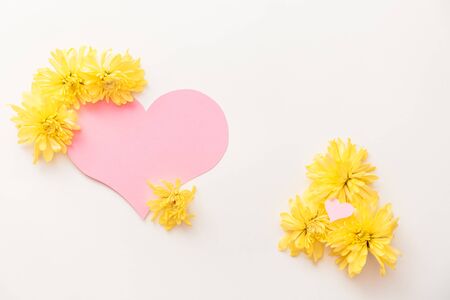 a large pink heart with a place for text decorated with yellow chrysanthemums on a white background, symbol of loveの写真素材