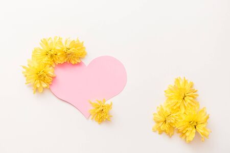 a large pink heart with a place for text decorated with yellow chrysanthemums on a white background, symbol of loveの写真素材