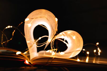 art book novel with sheets in the shape of a heart decorated with bright garland lights and...