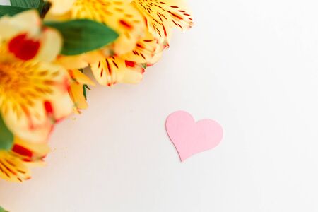 A pink heart with a place for text decorated with a yellow flowers on a white background, symbol of loveの写真素材