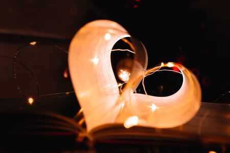 art book novel with sheets in the shape of a heart decorated with bright garland lights and...