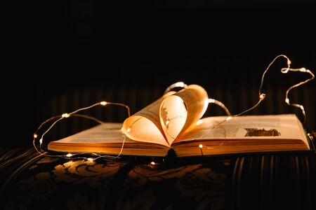 art book novel with sheets in the shape of a heart decorated with bright garland lights and...