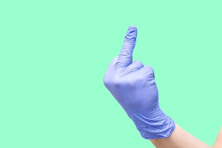 A hand with a blue latex glove isolated on mint background shows an obscene gesture with the middle...